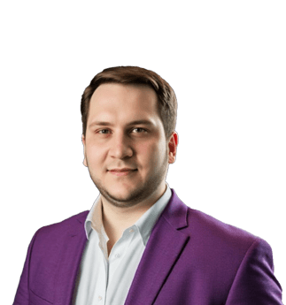 Mann mit kurzen braunen Haaren, der einen lila Blazer und ein weißes Hemd trägt, posiert und lächelt leicht vor einem schlichten weißen Hintergrund.