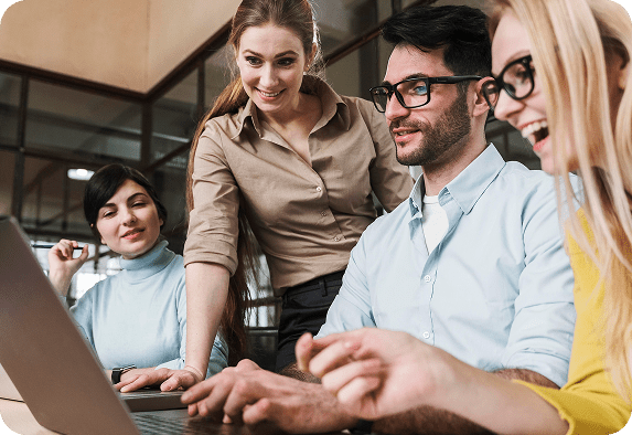 Vier Kollegen versammeln sich in einem modernen Büro um einen Laptop, lächeln und diskutieren angeregt über Basic Performance, was auf starke Teamarbeit und effektive Zusammenarbeit schließen lässt.