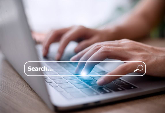 Nahaufnahme von Händen, die auf einer Laptoptastatur tippen, mit einer digitalen Suchleiste als Overlay, die die Online-Informationssuche anzeigt.